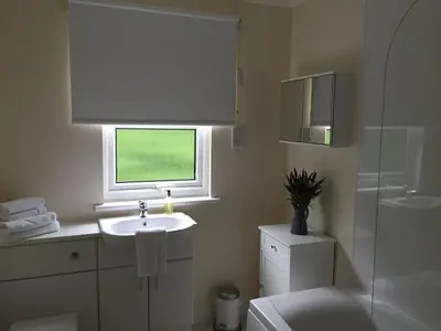 a white bathroom with a sink and a window at Bruce's Cottage in Stirling