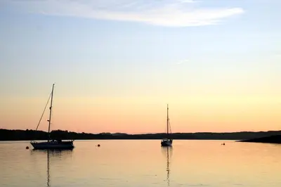 two boats sitting in the water at sunset at Loch Melfort Hotel in Ardfern