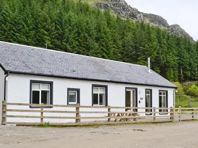 a white building with a wooden fence in front of a mountain at Corrie Massan in Benmore