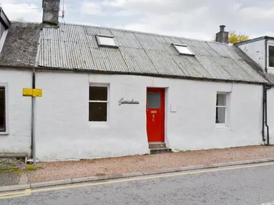a white house with a red door on a street at Gracedieu in Killin
