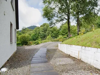 an empty road with a stone wall and trees at Bethany Cottage in Aberfoyle