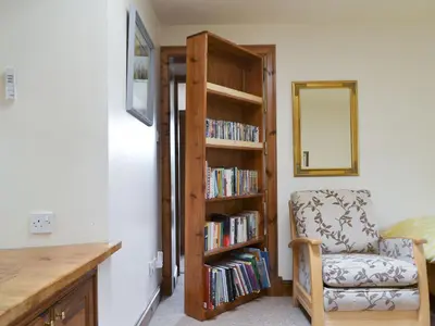 a room with a chair and a book shelf with books at Old Stones in Glendevon