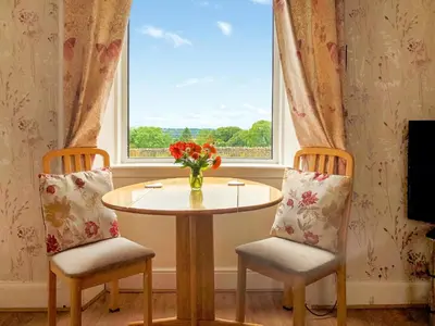 a table and two chairs with a vase of flowers in a window at Old Barn Farm Cottage - Cc in Uplawmoor