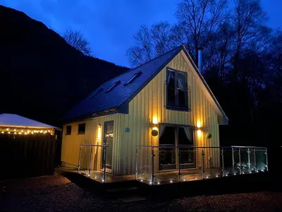 a house with lights on the side of it at night at Bluebell Cottage with Hot Tub in Ballachulish
