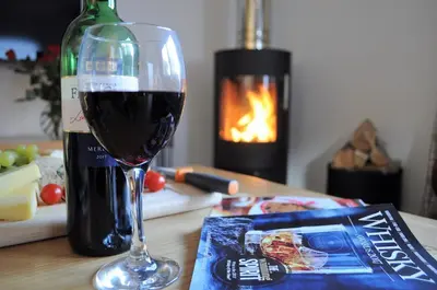 a glass of wine sitting next to a bottle of wine at Bluebell Cottage with Hot Tub in Ballachulish