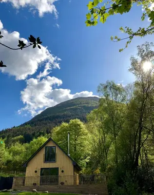 a cabin in the woods with a mountain in the background at Bluebell Cottage with Hot Tub in Ballachulish