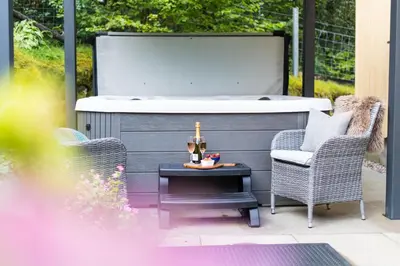a hot tub on a patio with two chairs and a table at Bluebell Cottage with Hot Tub in Ballachulish