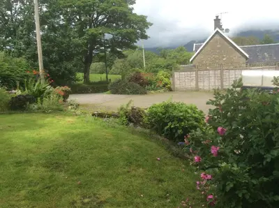 a house with a yard with flowers and a driveway at Riverside Cottage B&B in Cladich