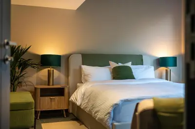 a bedroom with a bed with a green headboard and two lamps at Garden Rooms Edinburgh in Edinburgh