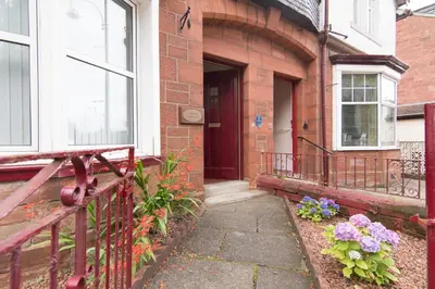 a brick house with a porch with flowers on it at Norwood Guesthouse-Loch Lomond in Balloch