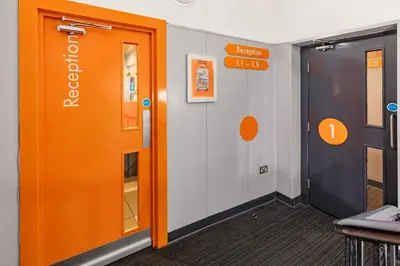 an office corridor with an orange door and exit sign at easyHotel Edinburgh in Edinburgh