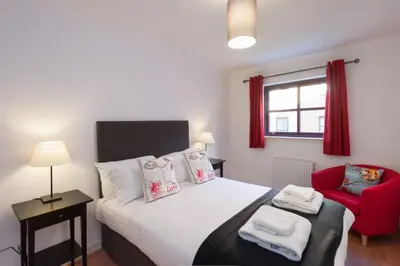 a bedroom with a bed and a red chair at Glasgow City Flats - Merchant City in Glasgow