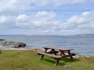a wooden picnic table sitting next to the ocean at The Shieling in Lochranza