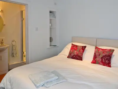 a white bed with red pillows and a towel on it at Roseburn Cottage in Moffat