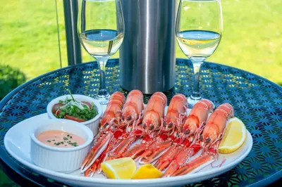 a plate of shrimp on a table with glasses of wine at Loch Linnhe Waterfront Lodges with Hot Tubs in Glencoe