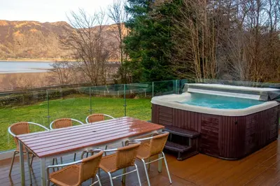 a hot tub on a deck with a table and chairs at Glenachulish Bay with Hot Tub in Glencoe