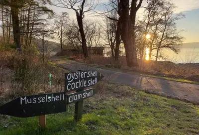 a sign in the grass next to a road at Cockleshell Lodge in Otter Ferry