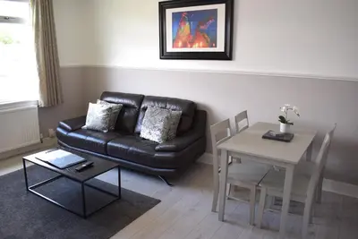 a living room with a black leather couch and a table at Kelpies Serviced Apartments - Wallace in Falkirk