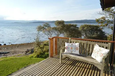a bench with two pillows sitting on a deck overlooking the water at Oystershell Lodge in Otter Ferry