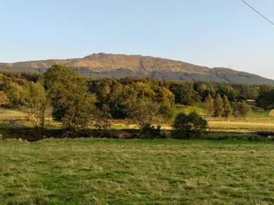 a field with trees and mountains in the background at Craignavie Cottage in Killin