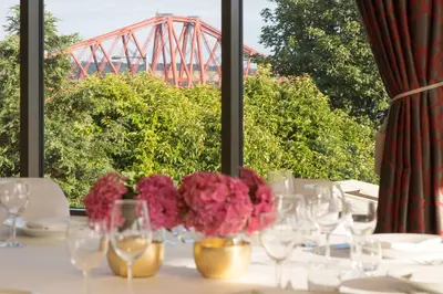 a table with pink flowers and a bridge in the background at DoubleTree by Hilton Edinburgh - Queensferry Crossing in North Queensferry