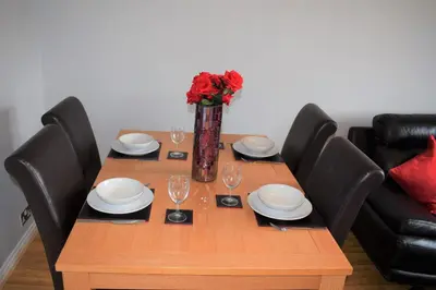a wooden table with chairs and a vase with red roses at Kelpies Serviced Apartments - McClean in Falkirk