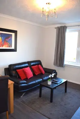 a living room with a black leather couch with red pillows at Kelpies Serviced Apartments - McClean in Falkirk