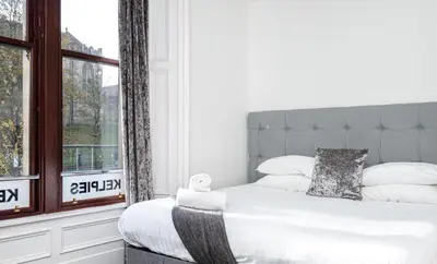 a bedroom with a white bed with a large window at Kelpies Serviced Apartments in Falkirk