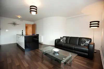 a living room with a black couch and a glass table at The Spires Serviced Apartments Glasgow in Glasgow