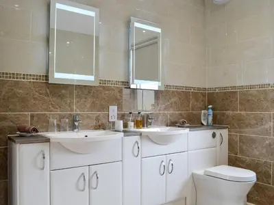 a bathroom with two sinks and a toilet and a mirror at Liftingstane Cottage in Closeburn