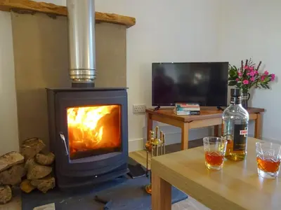 a wood stove in a living room with a table at Charlies Cottage in Muasdale