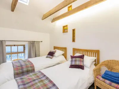 two beds in a room with a chair and a window at The Hayloft in Blitterlees