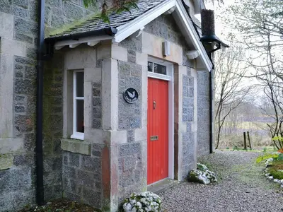 a red door on the side of a brick building at Craig Lora in Dalmally
