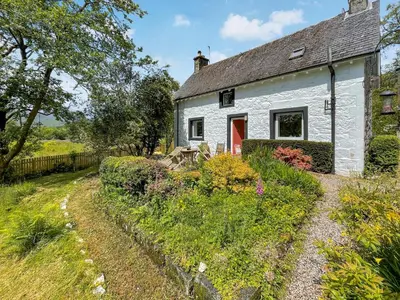 a white cottage with a red door in a garden at Craig Lora in Dalmally