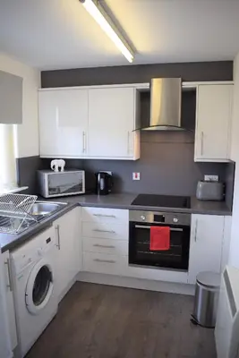 a kitchen with white cabinets and a washing machine at Kelpies Serviced Apartments Alexander- 2 Bedrooms in Falkirk