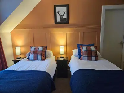 two beds in a hotel room with two lamps at The White Stag Inn in Strathyre