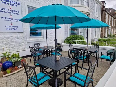 a patio with tables and chairs with umbrellas at Commodore Guesthouse, Seaside Holiday Suites in Rothesay
