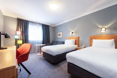 a hotel room with two beds and a chair at Holiday Inn Edinburgh Zoo by IHG in Edinburgh
