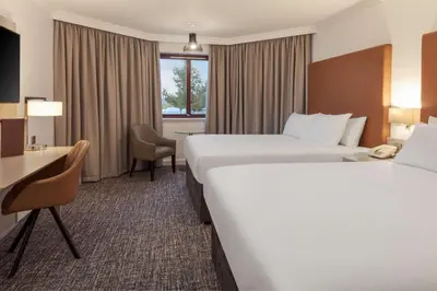 a hotel room with two beds and a desk at Glasgow Westerwood Hotel, Spa & Golf Resort in Cumbernauld