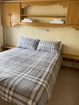 a bed with a blue and white plaid blanket at Curacao Caravans in Taynuilt