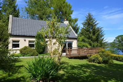a white house with a wooden deck in a yard at Alder Cottage in Blairmore