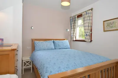 a bedroom with a bed with blue sheets and a window at Larch Cottage in Blairmore