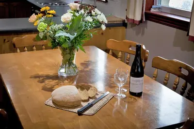 a table with a vase of flowers and a bottle of wine at Larch Cottage in Blairmore