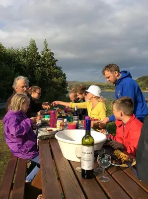 a group of people sitting at a picnic table with wine bottles at Oban Seil Farm The Bothy in Clachan
