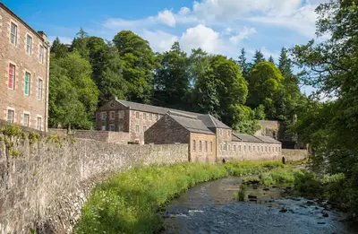 an old brick building with a river in front of it at New Lanark Mill Hotel in Lanark
