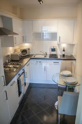 a kitchen with white cabinets and a glass table at Lexington Apartments in Rothesay