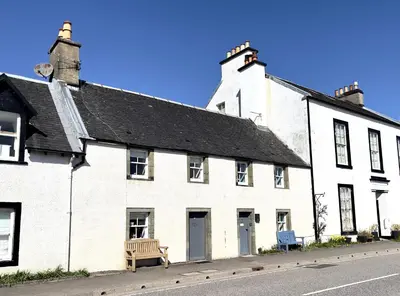 a white building with a bench in front of it at Newton Cottage North in Inveraray