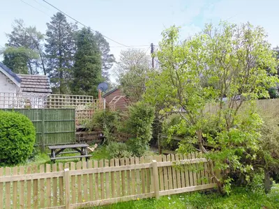 a wooden fence with a picnic table in a garden at Craigdarroch Cottage in Strathyre