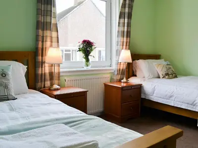 two beds in a room with a window and two lamps at Harbour View in Oban
