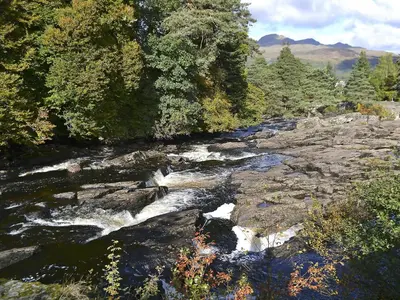 a river with rapids on the rocks and trees at Casa Duran in Killin